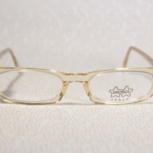 Könnte beinhalten: Klare, hellbraune Plastikbrille mit rechteckigem Gestell. Die Brille hat den Text "Luxottica Italy" auf der rechten Linse.
