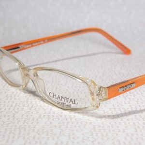 Pode incluir: Óculos transparentes com armação laranja, com a marca "CHANTAL occhiali" e "zero" impressos na lateral.