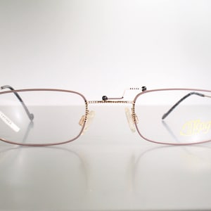 Könnte beinhalten: Eine Brille mit goldfarbenem Rahmen, braunem Gestell und klaren Gläsern. Die Brille hat einen kleinen goldenen Steg, der die beiden Gläser verbindet. Das Wort "Silhouet" ist auf dem rechten Glas sichtbar.