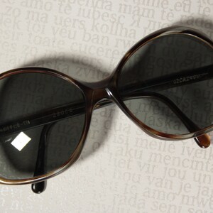 May include: Brown tortoise shell sunglasses with dark lenses. The sunglasses have a rounded, oval shape and a thin black frame. The text "28004" and "020A240" are printed on the frame.