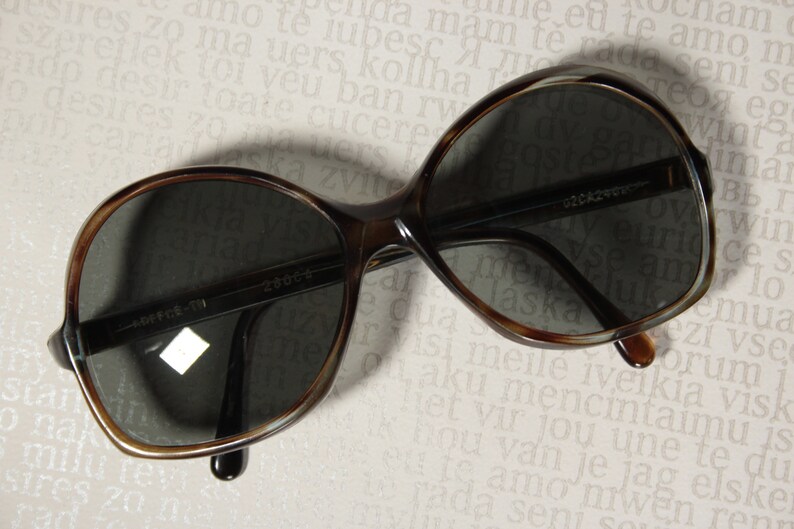 May include: Brown tortoise shell sunglasses with dark lenses. The sunglasses have a rounded, oval shape and a thin black frame. The text "28004" and "020A240" are printed on the frame.