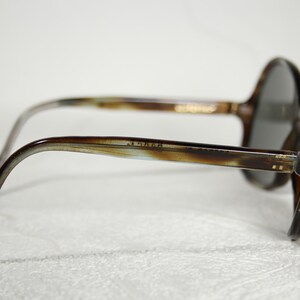 May include: Brown tortoiseshell sunglasses with round lenses and a thin metal bar across the bridge.