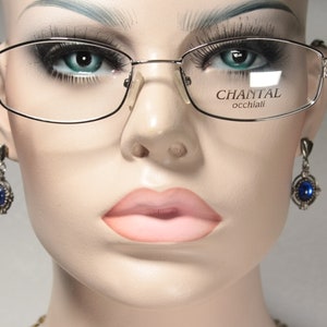May include: A pair of silver-framed glasses with clear lenses. The glasses have a subtle curve to the frame and the brand name "CHANTAL occhiali" is printed on the right lens.