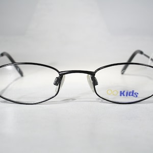 Puede incluir: Gafas de metal negro con montura y lentes transparentes. Las lentes tienen la palabra "OO Kids" impresa.