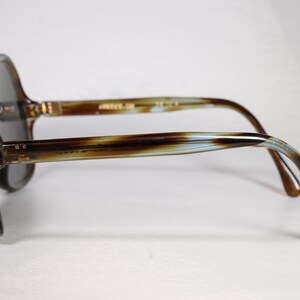 K&ouml;nnte beinhalten: Vintage &uuml;bergro&szlig;e Sonnenbrille mit braunem und beigem Schildpattmuster. Die Gl&auml;ser sind dunkelgrau. Die B&uuml;gel der Brille haben einen Farbverlauf aus Braun, Beige und Hellblau. Der Text "Javi After" ist sichtbar.