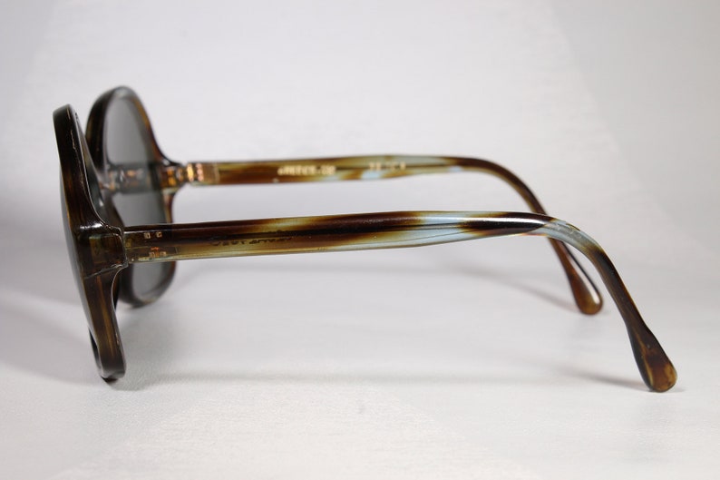 K&ouml;nnte beinhalten: Vintage &uuml;bergro&szlig;e Sonnenbrille mit braunem und beigem Schildpattmuster. Die Gl&auml;ser sind dunkelgrau. Die B&uuml;gel der Brille haben einen Farbverlauf aus Braun, Beige und Hellblau. Der Text "Javi After" ist sichtbar.