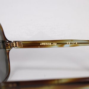 K&ouml;nnte beinhalten: Vintage Sonnenbrille mit Schildpattmuster und dunklen Gl&auml;sern. Der Rahmen hat ein klassisches Design mit einem Farbverlauf aus Braun und Beige. Der Text "GREECE-TM" und "52 [] 14" ist auf dem B&uuml;gel aufgedruckt.