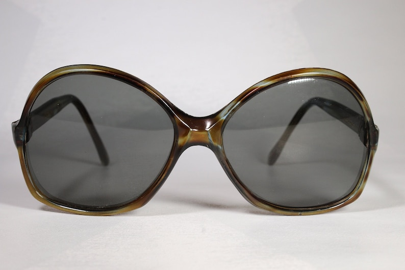 K&ouml;nnte beinhalten: &Uuml;bergro&szlig;e Sonnenbrille mit braunem und hellbraunem Schildpattrahmen und dunkelgrauen Gl&auml;sern. Die Sonnenbrille hat ein abgerundetes, schmetterlingsf&ouml;rmiges Design. Ein Vintage-Accessoire.