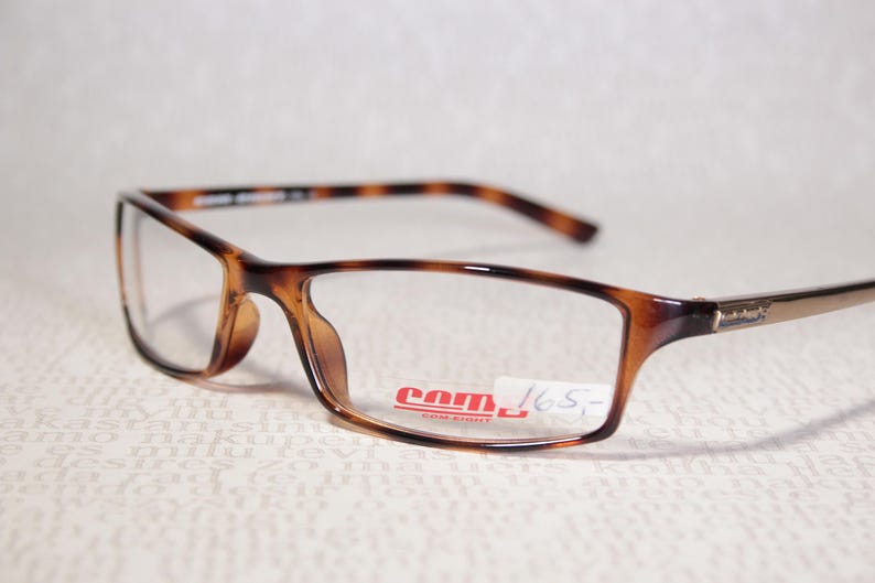 May include: Rectangular spectacles with a tortoiseshell pattern on the frames and arms. The lenses are clear, and the glasses have a small logo on the arm. A price tag is attached to the frame.