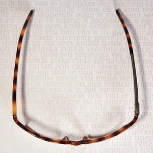 May include: Eyeglasses with a tortoiseshell pattern on the frames. The glasses are viewed from above, showcasing the shape and design of the frames. The background is a light colour with text.