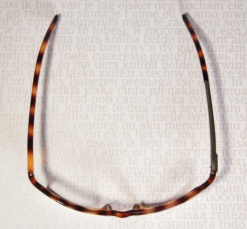 May include: Eyeglasses with a tortoiseshell pattern on the frames. The glasses are viewed from above, showcasing the shape and design of the frames. The background is a light colour with text.