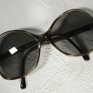 May include: Brown and tortoise shell sunglasses with dark lenses. The sunglasses have a rounded, oval shape.