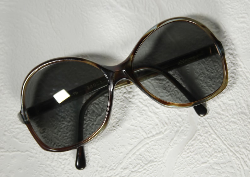 May include: Brown and tortoise shell sunglasses with dark lenses. The sunglasses have a rounded, oval shape.