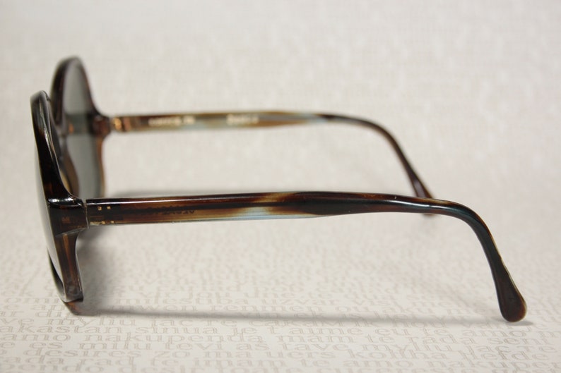 May include: Brown and blue tortoiseshell sunglasses with a rounded frame and thin arms.