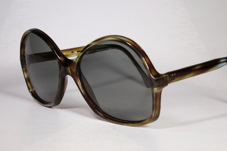 K&ouml;nnte beinhalten: &Uuml;bergro&szlig;e Sonnenbrille mit braunem Schildpattmuster-Rahmen und dunkelgrauen Gl&auml;sern. Die Sonnenbrille hat einen Retro-Vintage-Stil mit dickem Rahmen und breiten Gl&auml;sern. Die B&uuml;gel der Sonnenbrille sind ebenfalls braun mit Schildpattmuster.