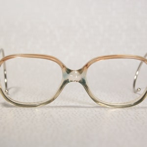 Peut inclure: Une paire de lunettes vintage avec une monture en plastique bleu et brun clair. La monture a une forme carrée arrondie et les branches sont fines et métalliques.