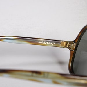 K&ouml;nnte beinhalten: Nahaufnahme einer Vintage-Sonnenbrille mit Schildpattmuster. Die Fassungen sind braun und beige mit einem hellblauen Akzent. Die Gl&auml;ser sind grau. Der Text "G2CA240" ist auf dem B&uuml;gel aufgedruckt.