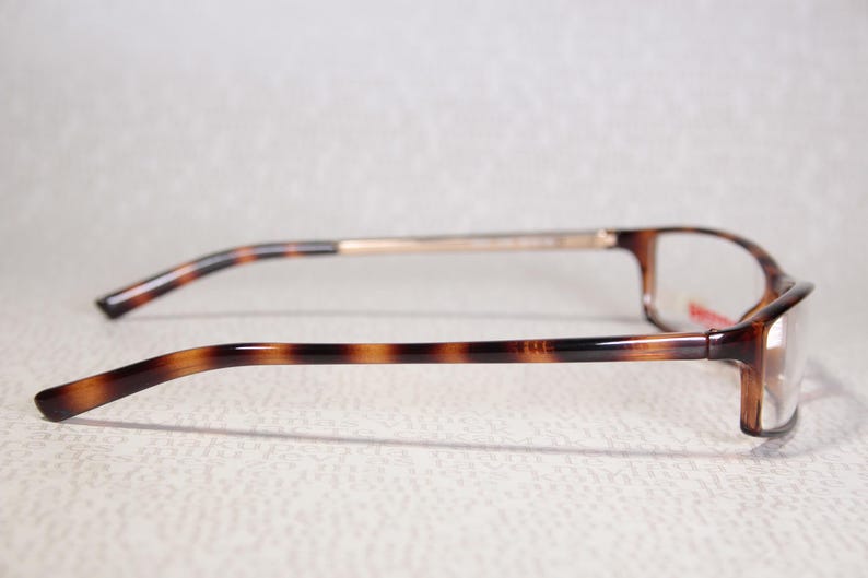 May include: Rectangular eyeglasses with a tortoiseshell pattern. The frames are brown and black. The temples have a similar pattern and connect to a gold-coloured bridge. The lenses are clear.
