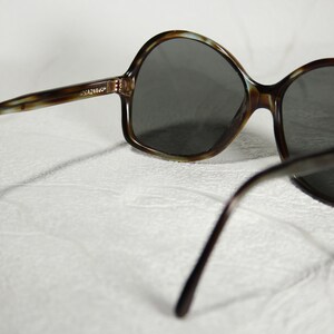 May include: Brown tortoiseshell sunglasses with dark gray lenses. The sunglasses have a rounded, oversized frame.
