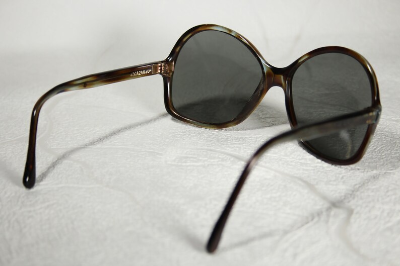 May include: Brown tortoiseshell sunglasses with dark gray lenses. The sunglasses have a rounded, oversized frame.