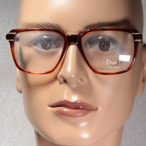 May include: A pair of tortoise shell eyeglasses with clear lenses. The glasses have a gold accent on the temples and the brand name "Atelier" is printed on the right lens.