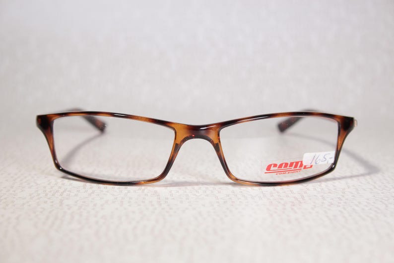 May include: Tortoiseshell pattern eyeglasses with clear rectangular lenses. The brand name "com" is printed in red on the lower right lens. The frame has a classic design. The glasses are suitable for everyday use.