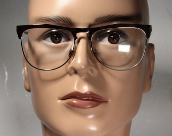 May include: Eyeglasses with a dark brown upper frame and a gold-coloured lower frame. The lenses are clear, and the glasses are set on a mannequin head. The glasses have a classic, retro style.