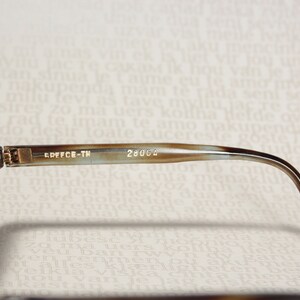 May include: Brown tortoise shell sunglasses with brown lenses. The sunglasses have a gold metal hinge and the text "EDFFCE-TH 28004" is printed on the arm.