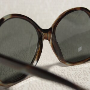 May include: Tortoise shell frame sunglasses with dark lenses. The sunglasses are on a white surface with printed text.