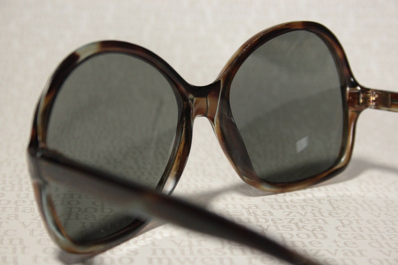 May include: Tortoise shell frame sunglasses with dark lenses. The sunglasses are on a white surface with printed text.