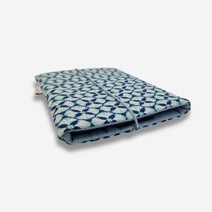 May include: A blue and white patterned fabric case with a blue elastic band closure. The case is folded closed and is lying on a white surface.