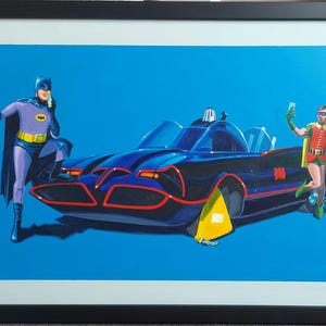 Puede incluir: Impresión enmarcada que presenta a Batman y Robin con el Batmóvil sobre un fondo azul. Batman viste un traje morado y negro, y Robin un atuendo rojo y verde. El Batmóvil es negro con detalles rojos.