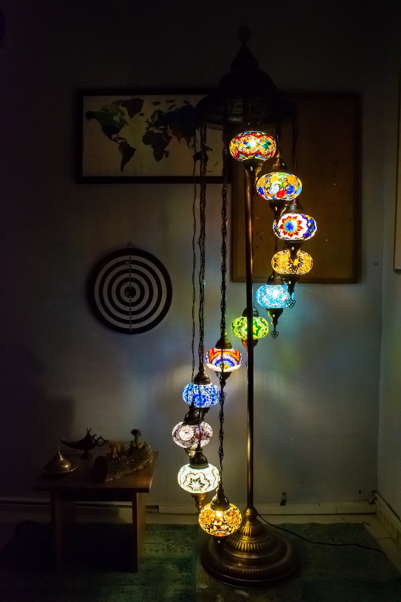 May include: A floor lamp with a spiral design features multiple colorful glass globes. The globes are decorated with intricate mosaic patterns in shades of blue, green, yellow, and red. The lamp is lit and casts a warm glow.