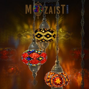 May include: Three hanging Turkish mosaic glass lamps with colourful geometric patterns. The lamps are suspended from a metal chain and have a brass finish.