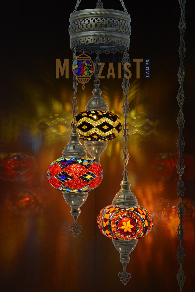 May include: Three hanging Turkish mosaic glass lamps with colourful geometric patterns. The lamps are suspended from a metal chain and have a brass finish.