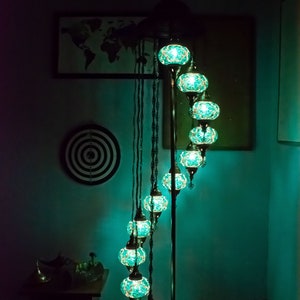 May include: A teal blue mosaic glass floor lamp with a spiral design and multiple lights. The lamp is on a dark surface in a room with a map on the wall.