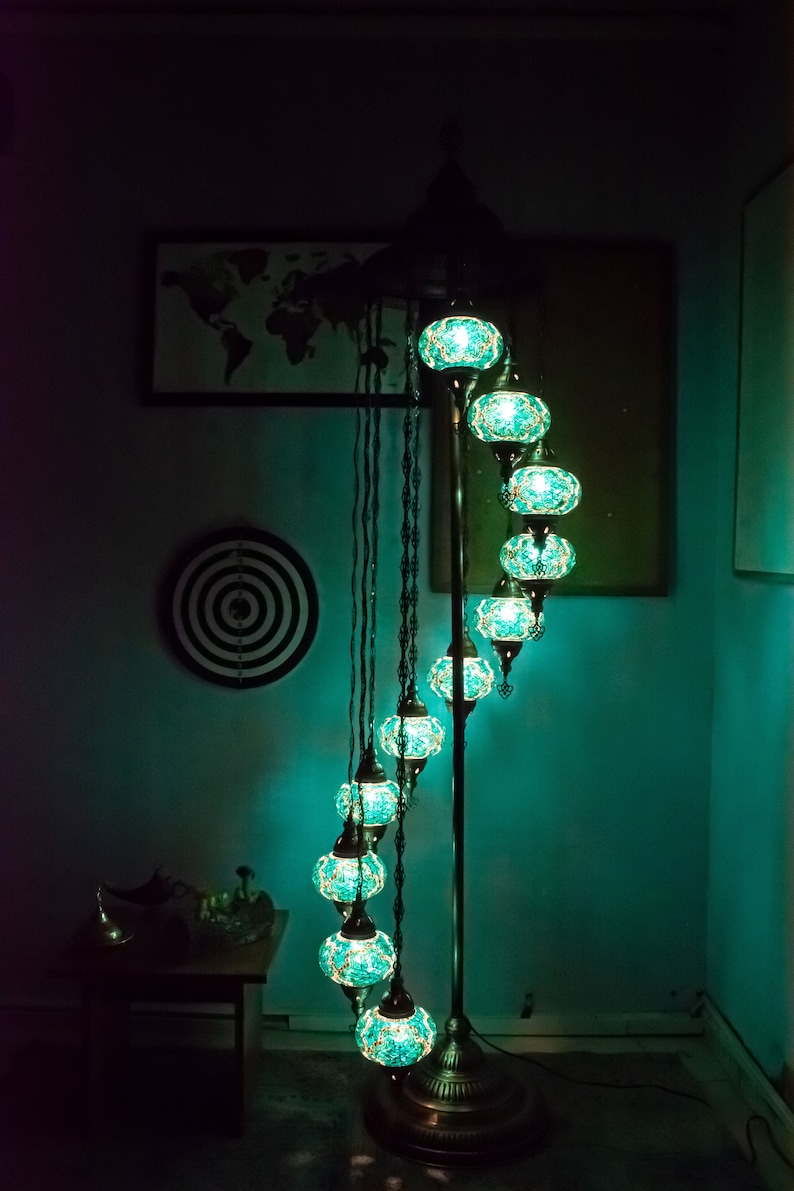 May include: A teal blue mosaic glass floor lamp with a spiral design and multiple lights. The lamp is on a dark surface in a room with a map on the wall.