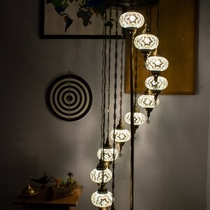 May include: A spiral floor lamp with a brass base and eight white mosaic glass globes. The lamp is lit and casting a warm glow.