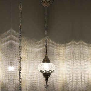 May include: A white glass pendant light with a brass chain and ornate brass accents. The light is on and illuminating the room.