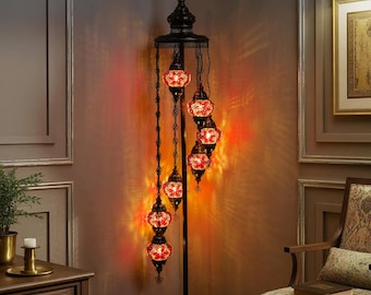 May include: A black metal floor lamp with six red and white mosaic glass globe shades. The lamp has a decorative top and base, and the shades hang at varying lengths. The lamp is in a room with a warm, inviting glow.