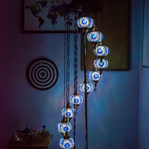 May include: A floor lamp with a spiral design features multiple blue and gold mosaic glass globes. The lamp is on a wooden floor and has a world map on the wall behind it.