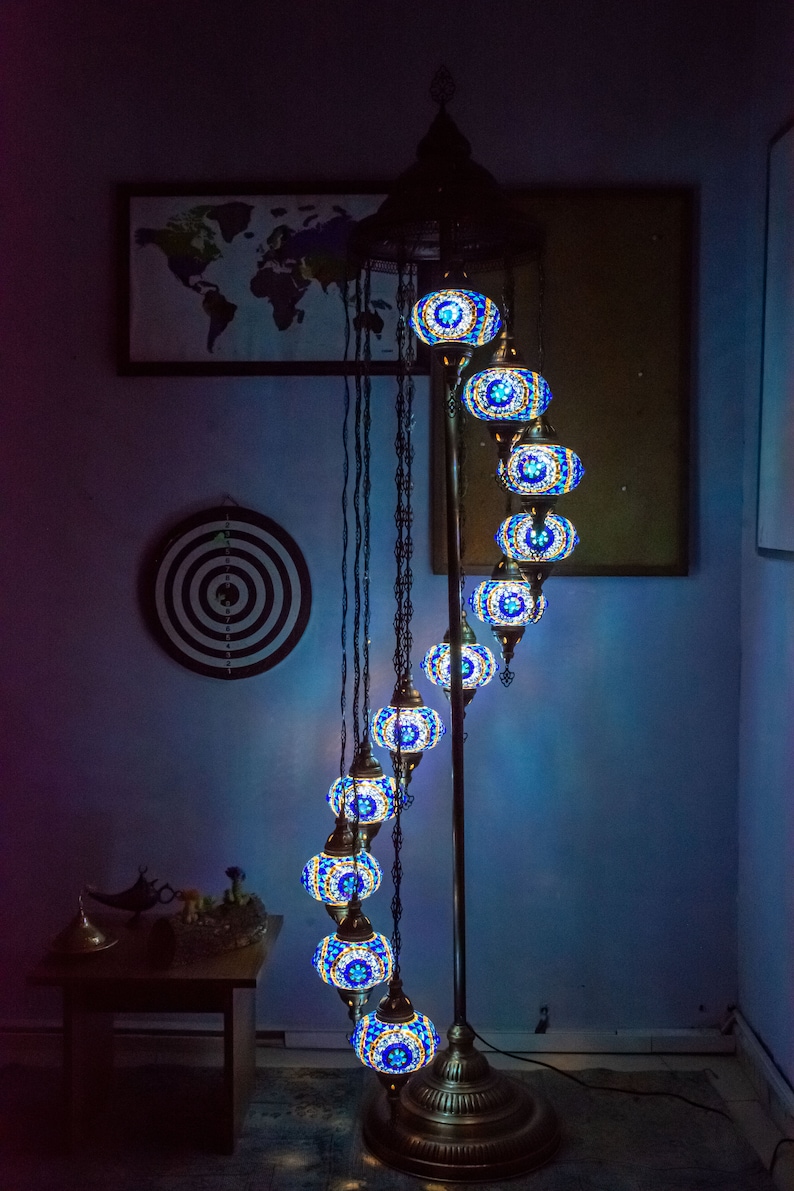 May include: A floor lamp with a spiral design features multiple blue and gold mosaic glass globes. The lamp is on a wooden floor and has a world map on the wall behind it.