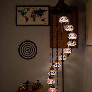 May include: A spiral floor lamp with a gold metal base and nine colorful glass globes. The globes are decorated with mosaic tiles in shades of blue, red, and orange. The lamp is lit and casting a warm glow.