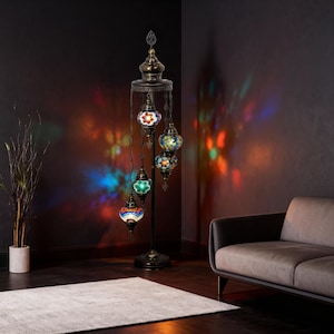 Może przedstawiać: Wysoka, ozdobna lampa podłogowa z pięcioma kolorowymi kloszami z mozaiki szklanej. Lampa ma ciemną metalową ramę i dekoracyjne zwieńczenie. Klosze w różnych kolorach, w tym czerwonym, niebieskim, zielonym i żółtym, rzucają kolorowe wzory światła na ścianę.