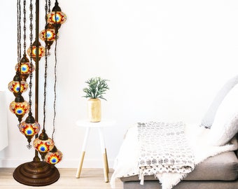 May include: A tall, spiral floor lamp with a dark metal base and multiple colorful glass globes. The lamp is lit and casts a warm glow. The lamp is in a living room setting with a couch and a side table.