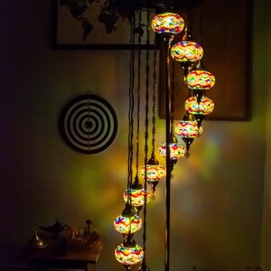 May include: A floor lamp with a spiral design features multiple colorful glass globes. The globes are made of mosaic glass and are illuminated with warm white light. The lamp has a dark brown metal base.
