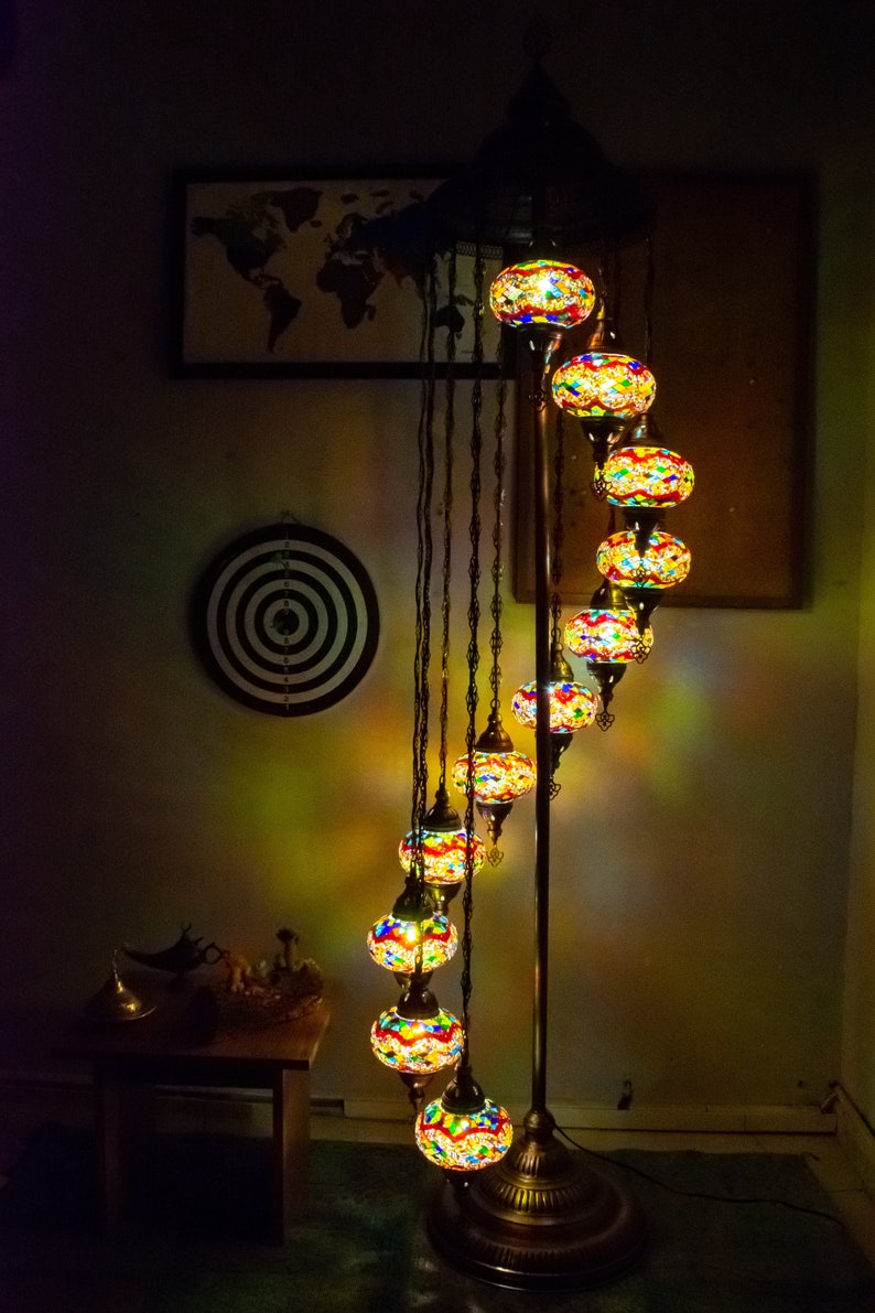 May include: A floor lamp with a spiral design features multiple colorful glass globes. The globes are made of mosaic glass and are illuminated with warm white light. The lamp has a dark brown metal base.