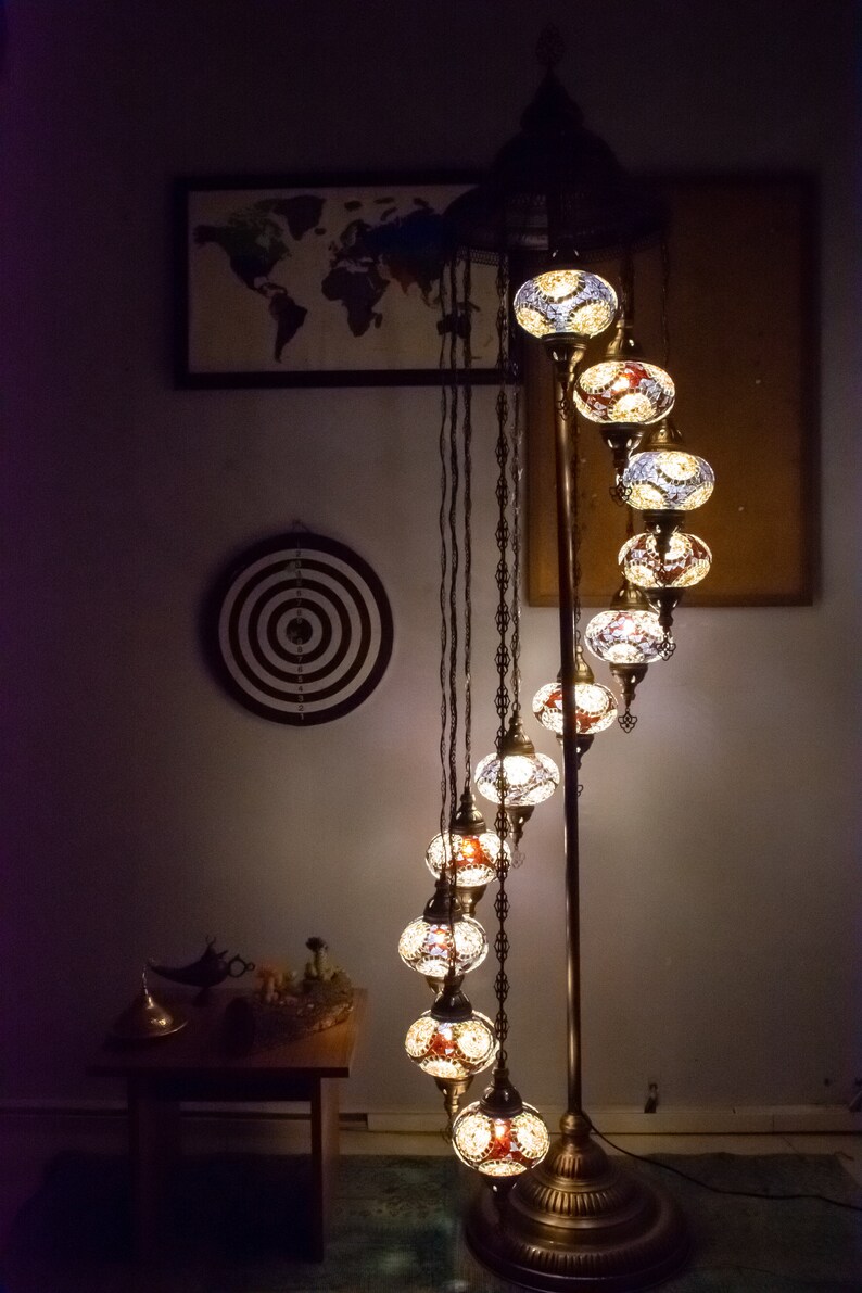 May include: A floor lamp with a curved design features a series of round, colorful glass globes. The globes are illuminated with warm white light. The lamp has a gold metal base and is standing on a dark brown rug.