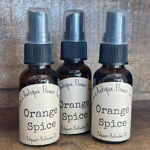 May include: Three brown glass spray bottles with black caps and clear plastic covers. Each bottle has a label that reads "Orange Spice Potpourri Refresher Oil" and "Julie's Antique Flower Fac".