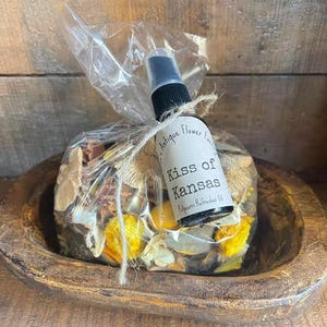 May include: A small brown wooden bowl filled with dried flower petals and a small bottle of "Kiss of Kansas" room refresher oil. The bottle is labeled "Antique Flower Essence".
